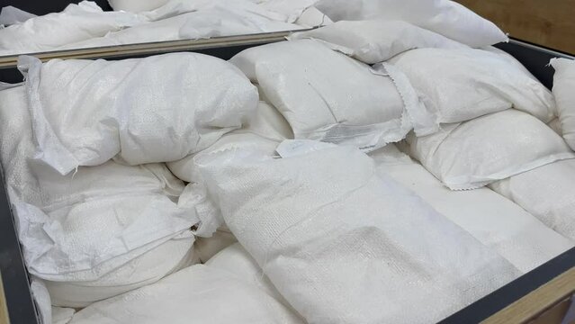 Packets of packaged white sugar stacked on top of each other for sale in a large supermarket. Sugar in bags of 25 kilograms in a deli. White bags with flour, sugar, groats or pasta products