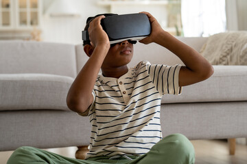 Curious African American kid boy wearing virtual reality 3D glasses online study simulation virtual...