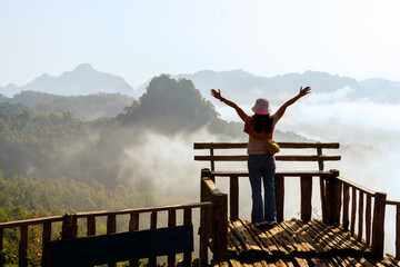 Happy woman raiseก open arms arms in morning light with background of mountains scenary in Chiangmai Thailan, lifestyle and healthy confidence relax woman travel concept.