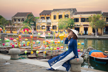 Asian woman is wearing Ao Dai traditional Vietnamese dress and traveling at Hoi An old town in Vietnam.