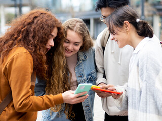 Group of teenage friends having a good time while looking at the smartphone in a city. Young...