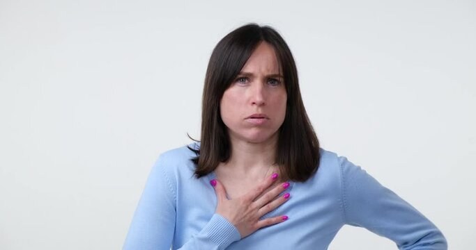 A Caucasian woman standing on a white background stares intently at the camera, suddenly getting startled and showing a shocked reaction. Her facial expression changes quickly from calm to scared.