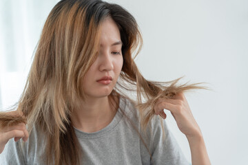 Asian woman very sad and upset looking at damaged hair, hair loss, hair thinning problem, vitamin...