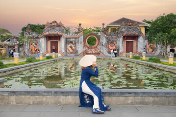 Asian woman is wearing Ao Dai traditional Vietnamese dress and traveling at the Ba Mu Temple Gate, Hoi an old town in Vietnam.