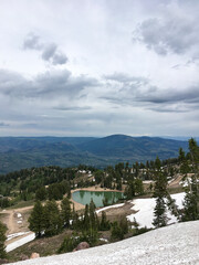 On summit of a mountain looking down onto a valley and emerald coloured lake, pine trees and stormy clouds. View of Wasatch Mountains, Little Cottonwood Canyon, Utah.