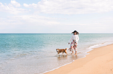 Beautiful fashionable young girl walking on the beach barefoot with her dog