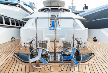 The bow of the yacht with teak deck, with anchor stops, part of the anchor chain, winch for tightening and ship bell made of stainless steel.