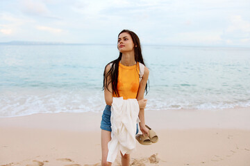 A young woman after swimming in the ocean with a backpack in wet clothes walks along the beach, summer vacation on an island by the ocean in Bali sunset