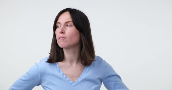 Caucasian woman stands on a white background, putting her hand to her forehead, looking for something, glancing around. In the end, she turns to the camera and shrugs her shoulders in uncertainty.