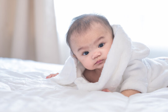 Adorable asian baby looking away with tpwel cover over head, lay on bed with sleepy feeling.
