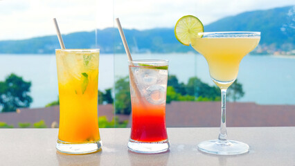 Refreshing tropical fruit cocktails by the hotel swimming pool with a sea view. Three vibrant-colored blended drinks in glasses, perfect for a summer getaway.