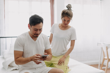 Funny asian couple. Wife peeking husband who chatting on the smartphone.