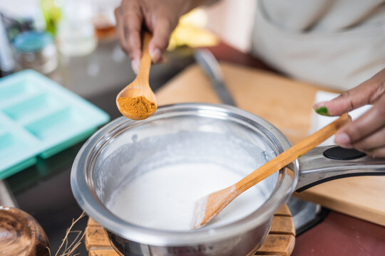 Female hands holding a wooden spoon next to a pot in the kitchen. Elaboration of organic soap based on glycerin.