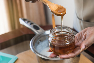 Female hands holding a bowl of bee honey and a wooden spoon. Close up. Elaboration of organic soap...
