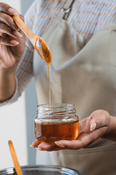 Female hands holding a bowl of bee honey and a wooden spoon. Close up. Elaboration of organic soap based on glycerin.