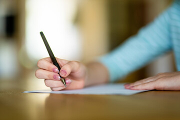 Close-up of woman's hands writing on a sheet of paper placed on a table.