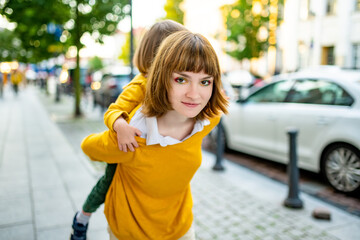 Cute big sister cuddling with her toddler brother. Adorable preteen girl piggybacking her small sibling. Children with large age gap.