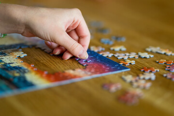 Close-up on woman hand playing puzzles at home. Connecting jigsaw puzzle pieces in a living room...