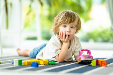 Cute toddler boy playing with blocks construction toy set on the floor at home. Daytime care creative activity. Kids having fun with toys. Educational learning games.