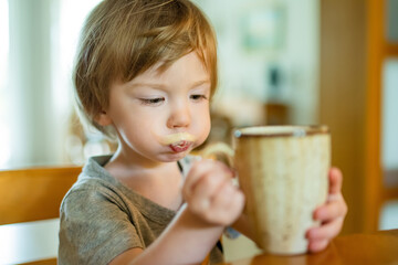 Cute toddler boy drinking decaffeinated coffee at home. Small child drinking hot beverage indoors.