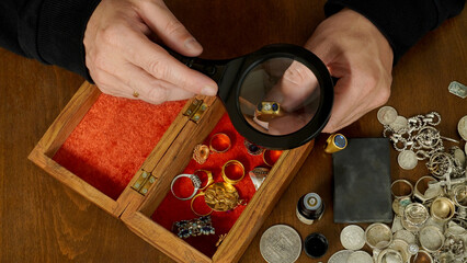 the jeweler, through magnifying glass, examines a ring with a diamond, against the background of a...
