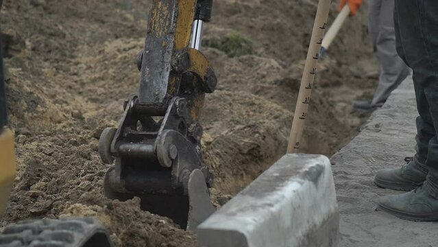 Excavator in action at the construction site. Stock footage. Bottom view of excavator flipping the bucket of yellow color loaded with sand on blue cloudy sky background.