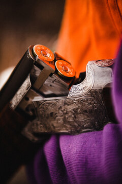 An antique silver shotgun beinbg loaded, shells reflecting an orange hunting vest, closeup macro