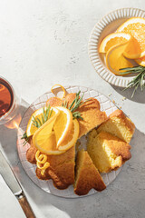 Sliced fluffy orange cake decorated with fresh orange slices on ceramic on light gray textured background, sunny morning breakfast in harsh light. Text space, flat lay, top view