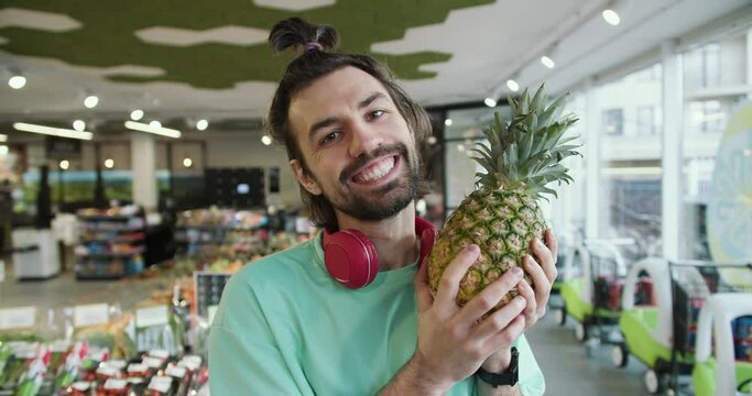 Playful Pineapple Fun: Young Man's Hilarious Antics in Green T-Shirt at the Supermarket