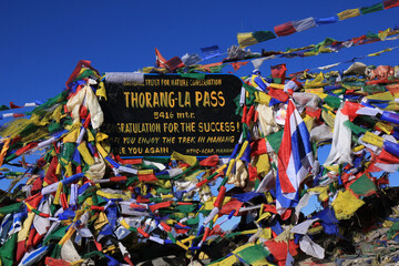 Colorful prayer flags and signboard on the Thorang La mountain pass, Nepal.