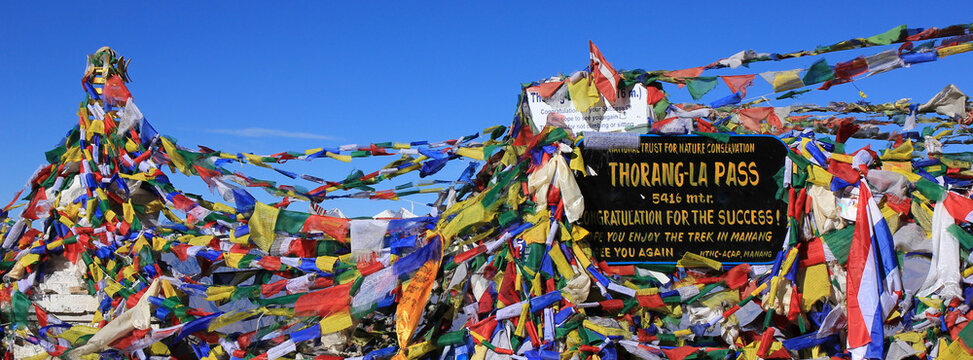 Prayer flags and signboard on the Thorang La mountain pass, Nepal.