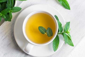 Cup of mint tea with fresh green mint leaves on rustic table, healthy herbal hot drink