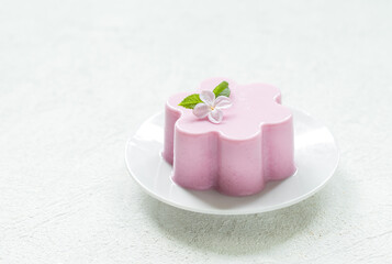 Obraz na płótnie Canvas Pink tea matcha cream pudding, Panna Cotta, decorated with a small flower. On a plate. Creamy dessert with the addition of pink pitahaya powder. White background. Copy space