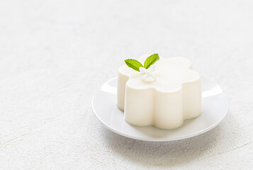 Vanilla cream pudding, Panna Cotta, decorated with white flower. On a plate. White background. Copy space
