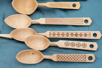 Ukrainian handmade carved wooden spoons with burnt ornament lying on a blue cloth.