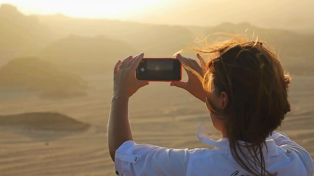 Young woman (back view) taking picture of sunset in desert, Sinai, Egypt