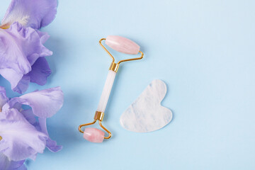 Modern selfcare concept. Pink jade roller and gua sha for face massage with flowers irises. Facial...