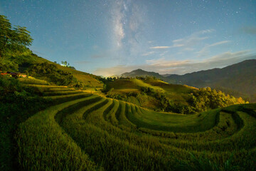 Fresh paddy rice terraces and milky way and stars on space, green agricultural fields in countryside or rural area of Mu Cang Chai, mountain hills valley in Asia, Vietnam. Nature landscape at night.