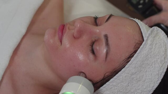 Massaging facial skin of a young woman using a cosmetology device