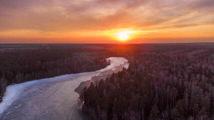 Winter sunset above winter forest with small rive