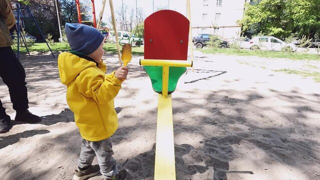A small child throws sand with a toy shovel on a swing. Concepts of education, exploration of the surrounding world, aggression, bad behavior, emotions, safety rules, physical development, psychology