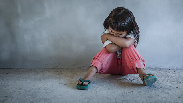 Sad little child girl sitting alone on floor concrete wall background