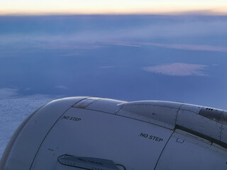 客席の窓から見た飛行中の旅客機のジェットエンジンと夕空