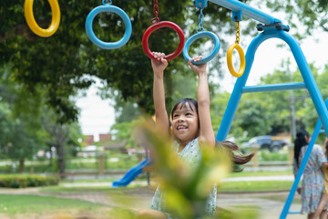 Happy girl hanging on monkey bar by hand doing exercise. Little Asian girl playing at outdoor...