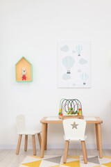 Table and chairs with toys near white wall in playroom. Stylish kindergarten interior