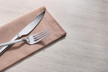 Shiny fork, knife and napkin on white wooden table, closeup. Space for text