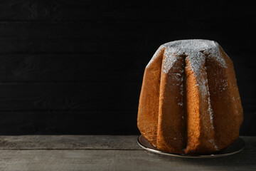 Delicious Pandoro cake decorated with powdered sugar on wooden table against black background, space for text. Traditional Italian pastry