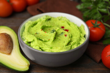 Bowl of delicious guacamole and ingredients on wooden table, closeup