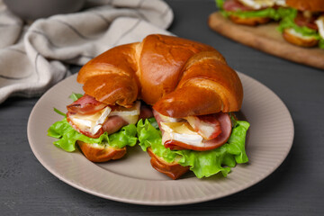 Tasty crescent roll with brie cheese, ham and bacon on grey wooden table, closeup