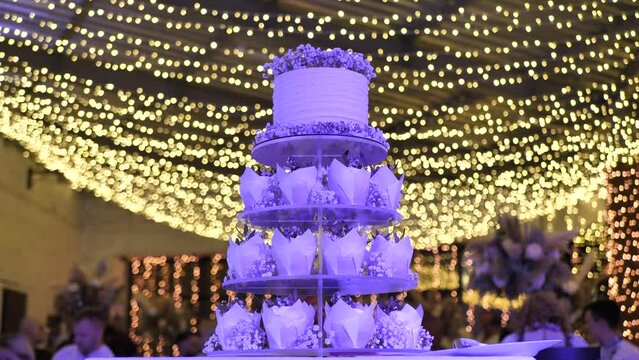 Wedding cake with cupcakes in the rays of blue spotlights. Delicious cake bar at a wedding